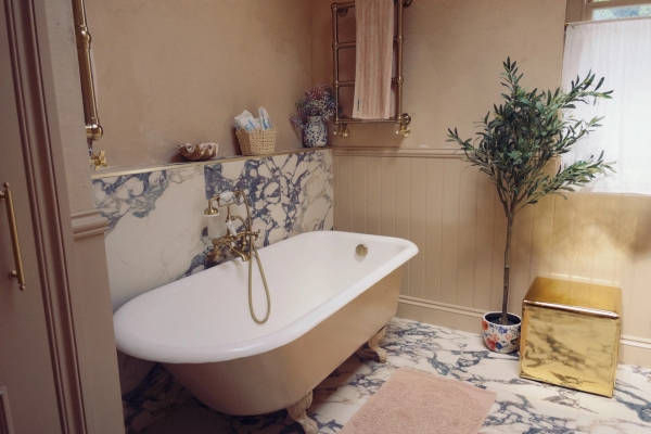 Luxurious bohemian bathroom featuring a classic white freestanding clawfoot bathtub, wooden wall panelling, and a patterned mosaic floor, Love Locations TW7.