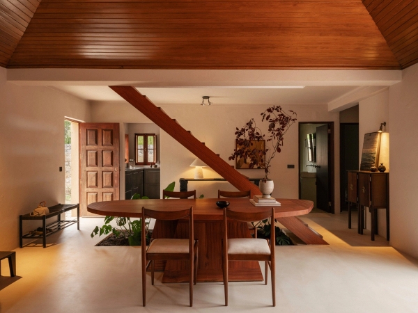 Warm open-plan living room with wood-clad ceiling, central timber dining table, and open staircase in Portugal, Love Locations 2705-064.