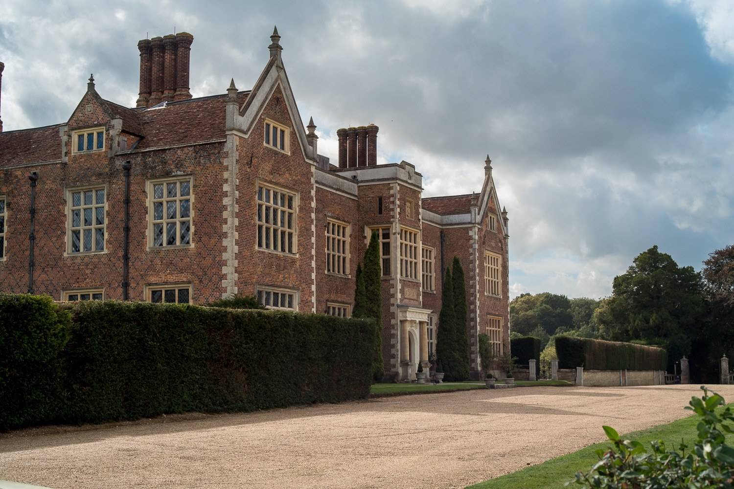 Impressive side facade of North Mymms Park manor house with gravel driveway and manicured hedging through Love Locations.
