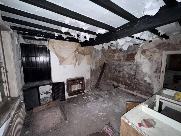 Abandoned cottage kitchen featuring charred-effect black beams, peeling floral wallpaper, and debris, a creepy movie set managed by Love Locations.