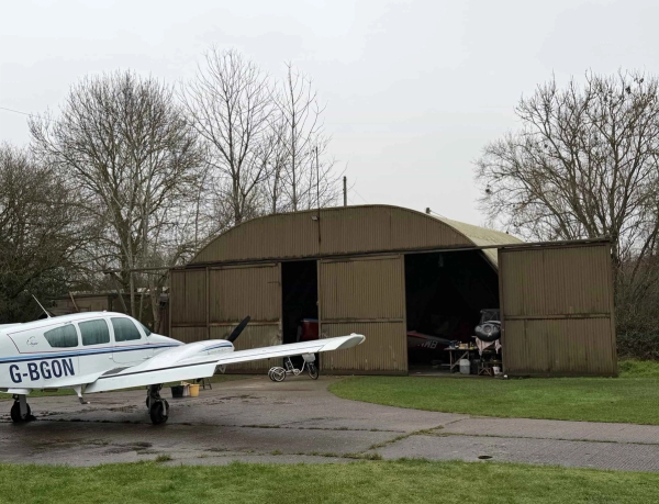 Aircraft hangar doorway with parked planes and maintenance equipment on a historic airfield location, Love Locations NN17.