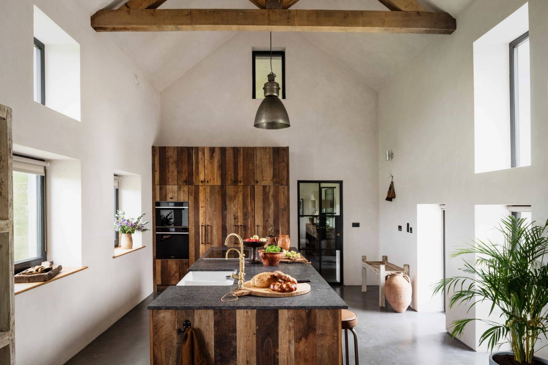 Open-plan kitchen location house in Castleblayney County Monaghan Ireland via Love Locations, showcasing dark timber cabinets, high vaulted ceilings, hanging pendant lights, and a kitchen island.