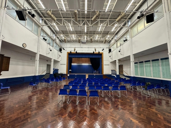 Love Locations school assembly hall location EN4: Wide shot of a spacious school theater room showcasing a polished parquet wood floor and dark blue curtains, perfect for multi-camera video shoots.