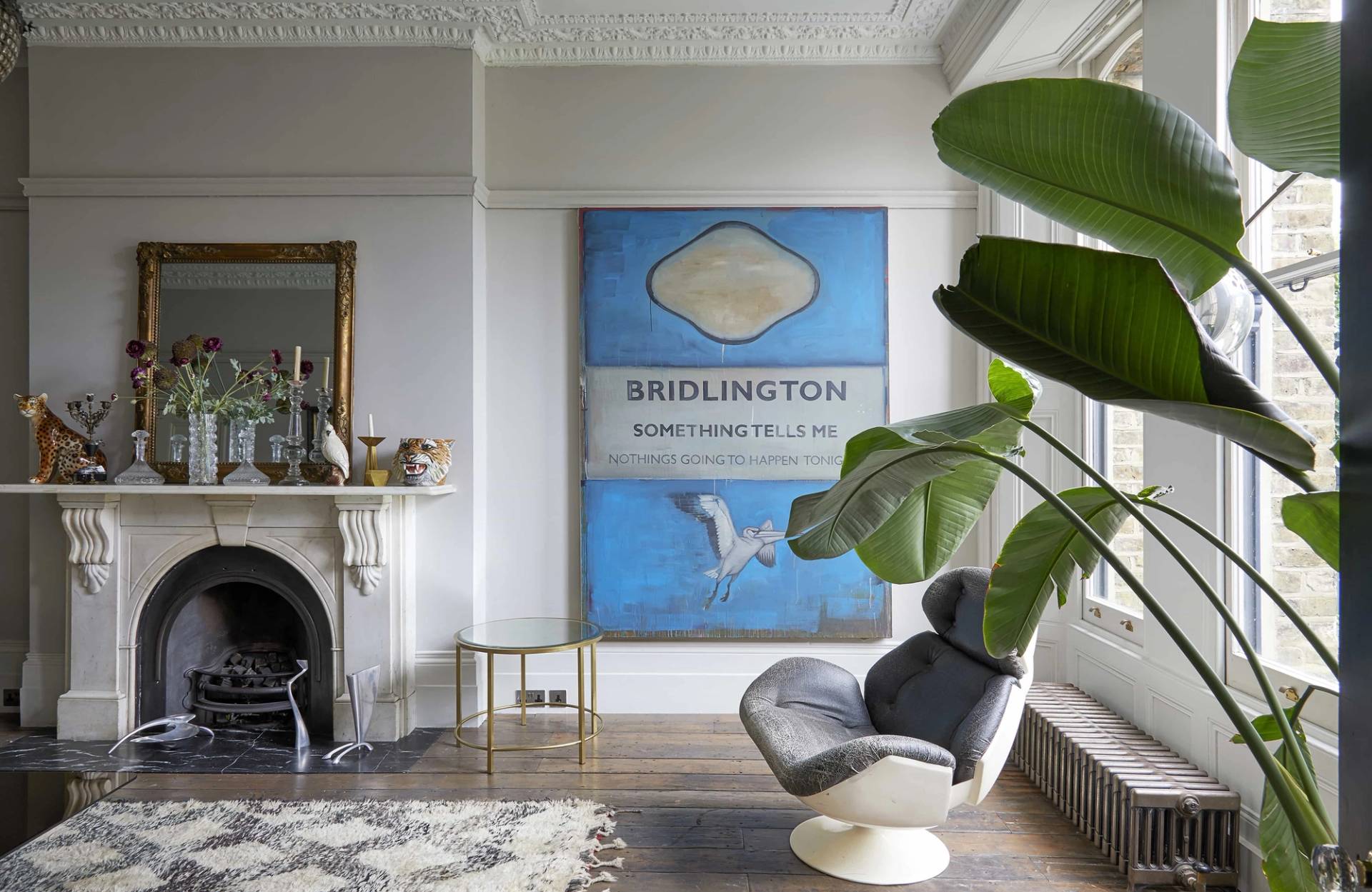 Ornate white marble fireplace hearth styled with vintage brass accents and blue travel poster in N16, Love Locations.