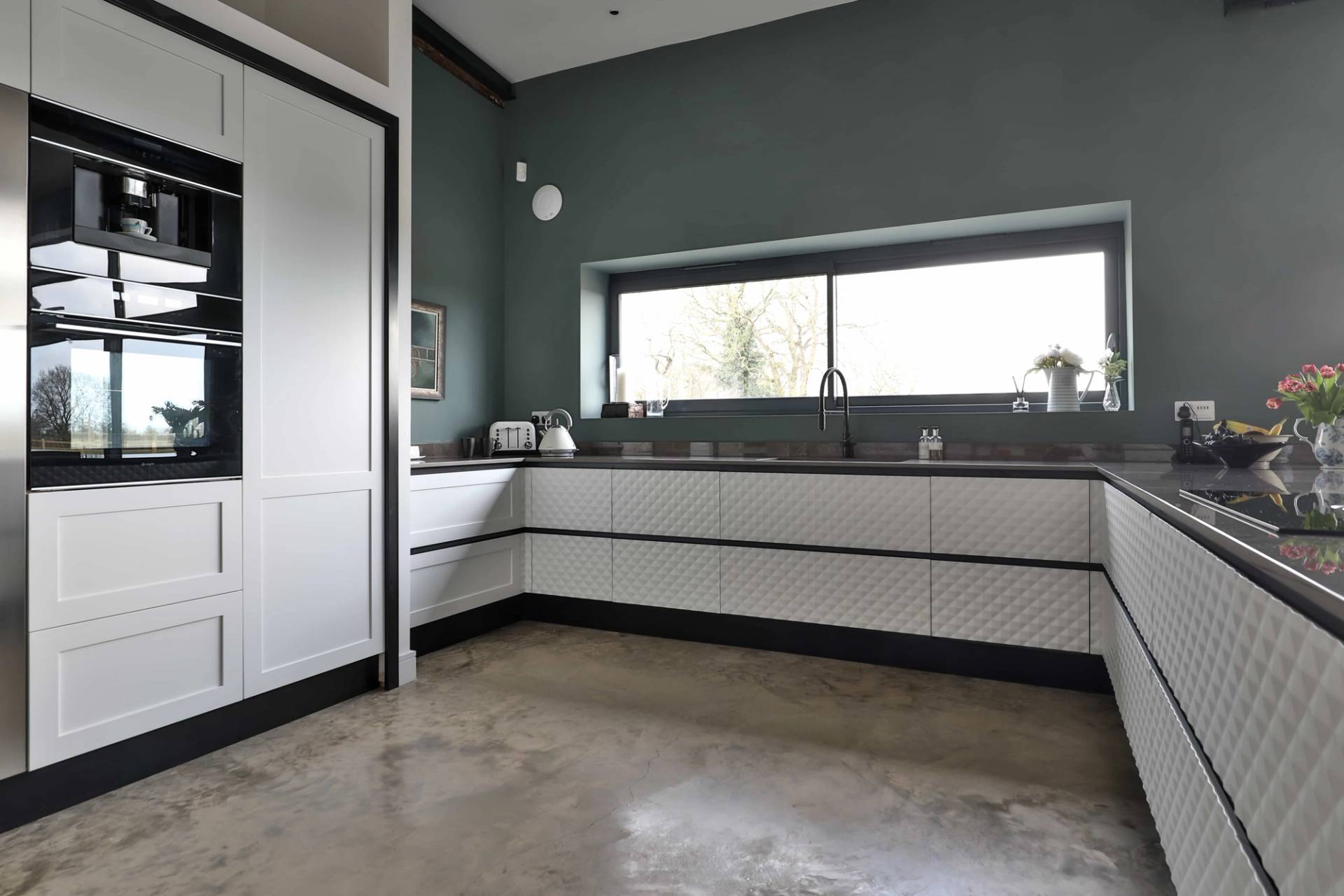 Modern L-shaped kitchen layout with dark teal walls, white quartz countertops, and horizontal splashback window, Love Locations CV23.