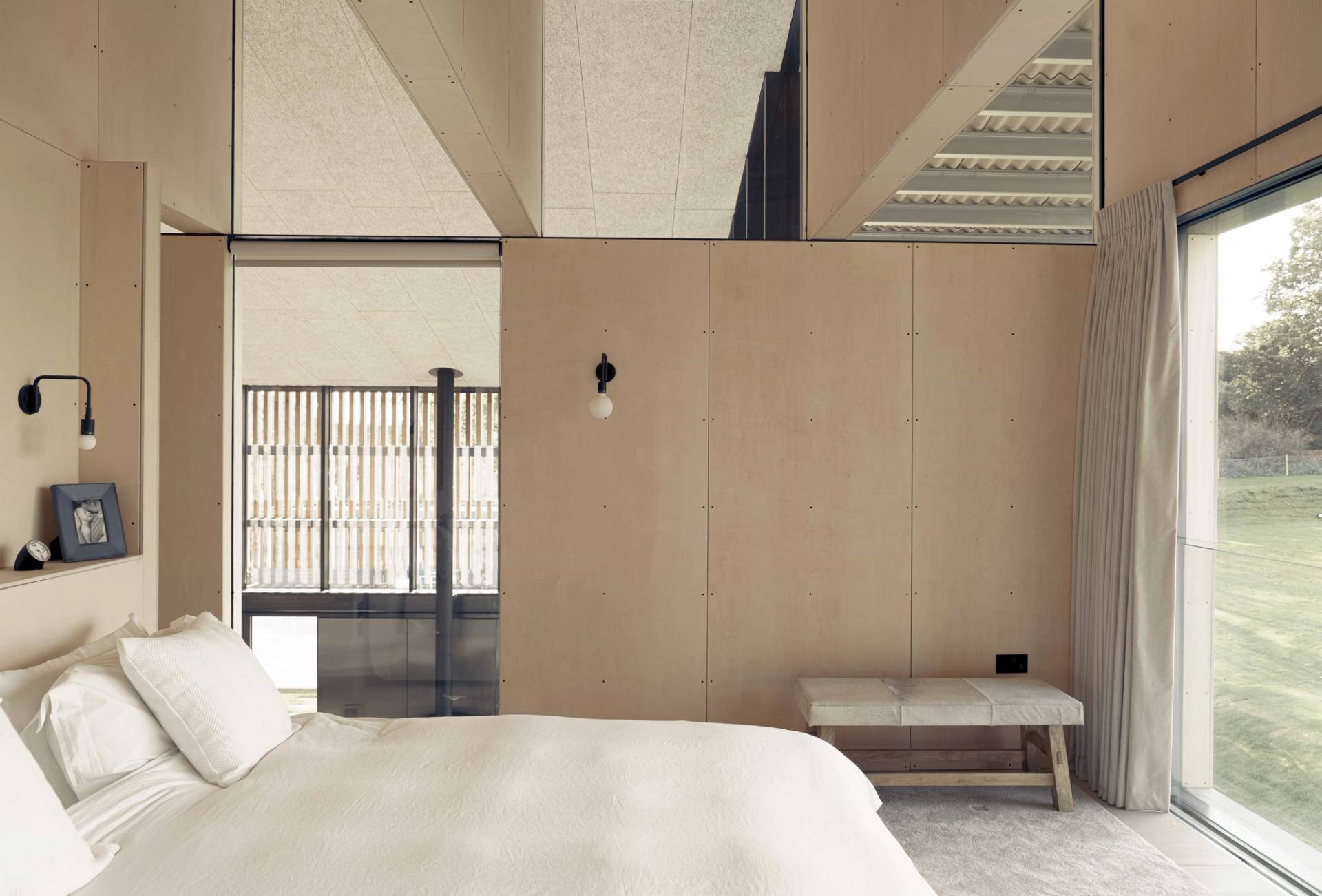 Minimalist master bedroom suite featuring natural wood wall cladding, neutral linen bedding, and a soft bench, Love Locations NR9.