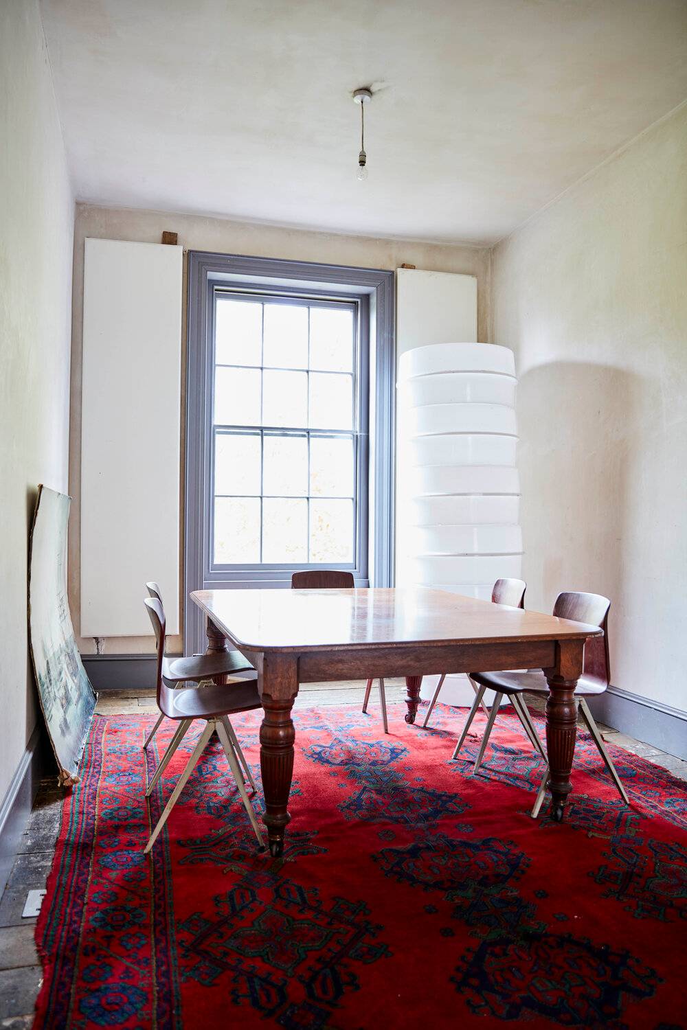 Minimalist dining room with a wooden table, red patterned rug, sash window, and raw plaster walls, ideal for editorial media filming, Love Locations SE8.