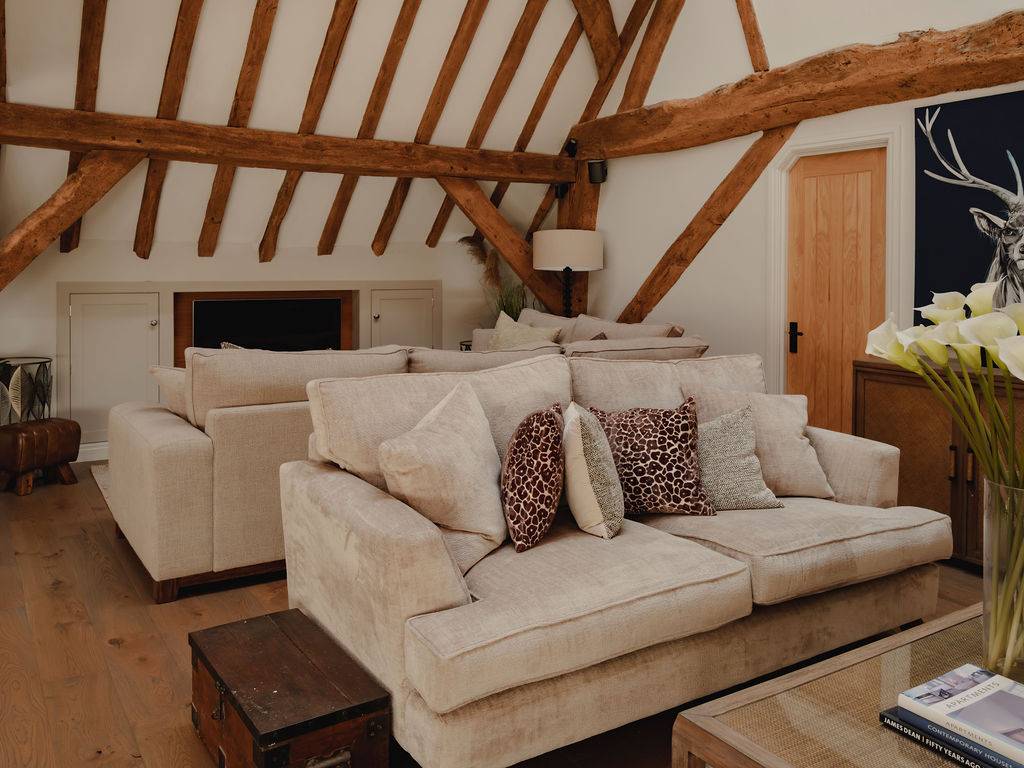 Upper mezzanine level seating area featuring deep cream sofas and rustic timber rafters in a Nuffield barn conversion, Love Locations RG9.
