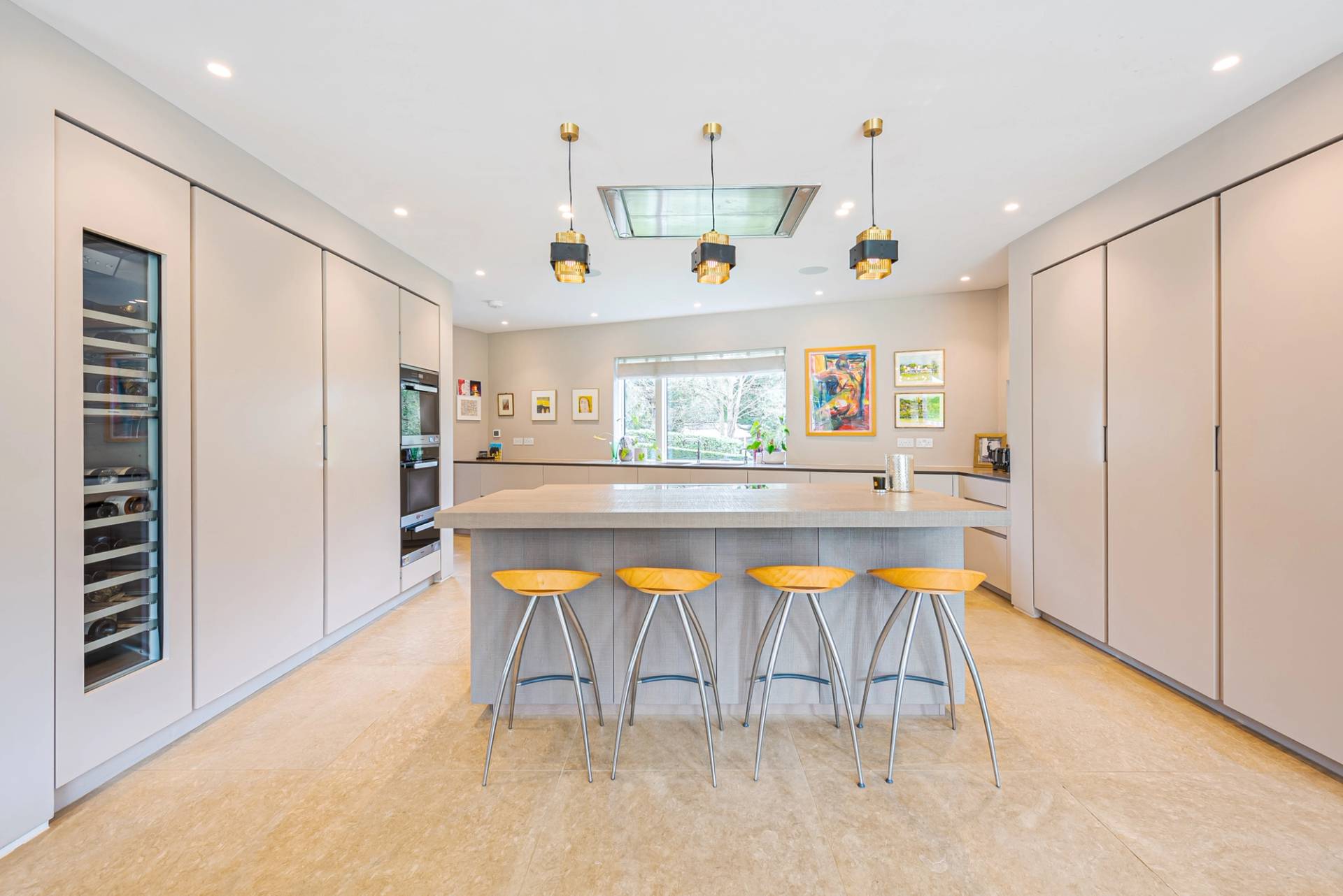 Luxury modern kitchen featuring a wide beige marble island counter, yellow leather bar stools, and skylight windows, Love Locations KT2.