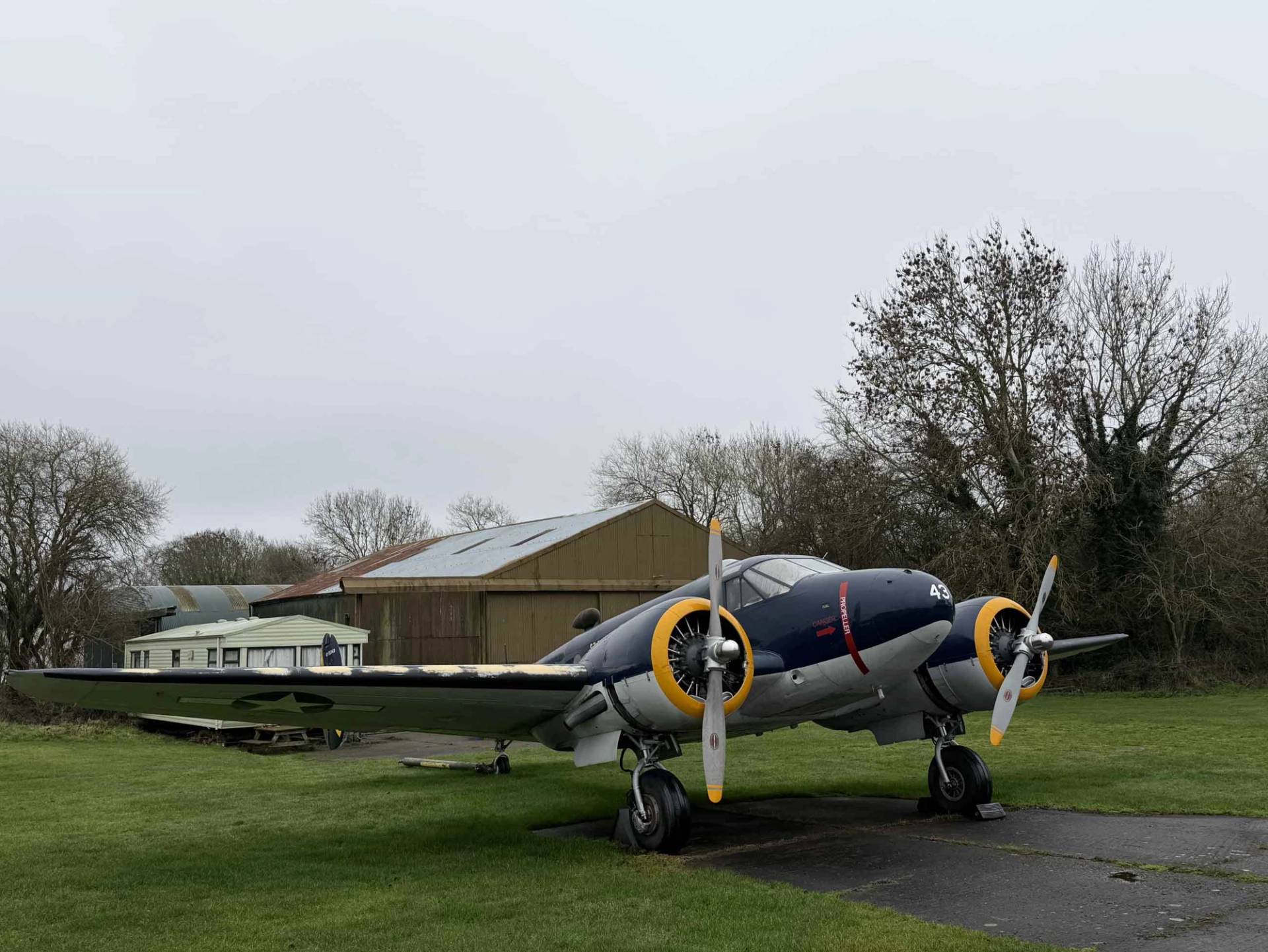 Twin-engine vintage aircraft parked outside an aviation hangar on a historic airfield location in Northamptonshire, Love Locations NN17.