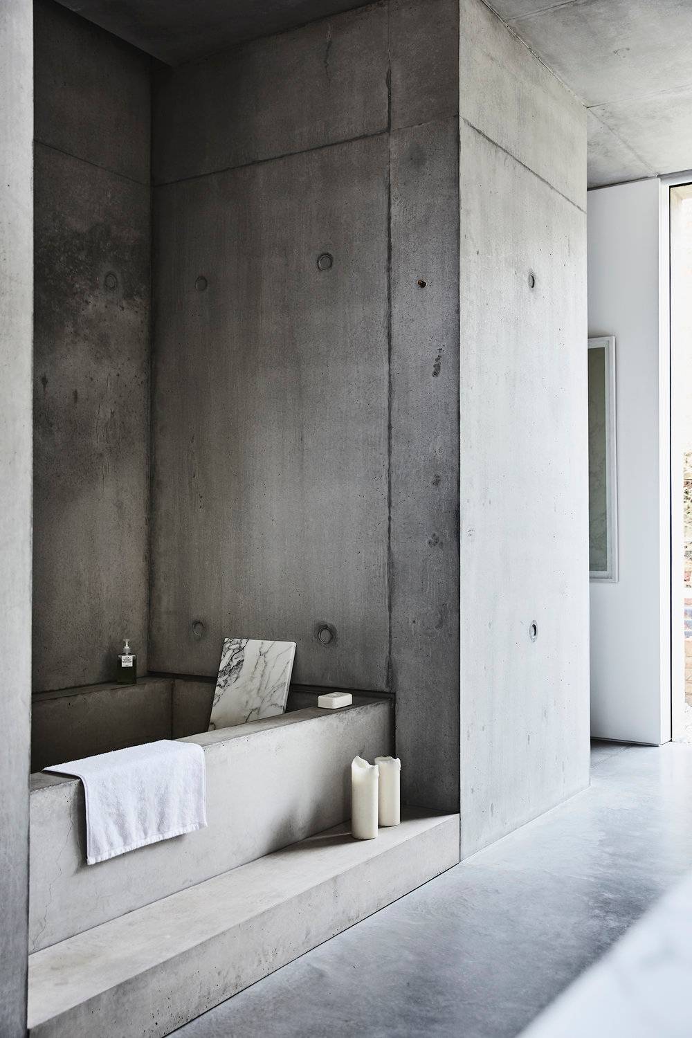 Monolithic raw concrete sunken bathtub nook with integrated wall alcoves and polished concrete finishes, perfect for luxury skincare and spa product commercials, Love Locations.