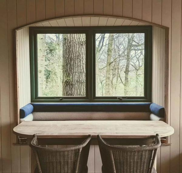 Bespoke wooden dining table and bench seating arranged perfectly in front of a large window viewing a massive tree trunk, unique production set via Love Locations.