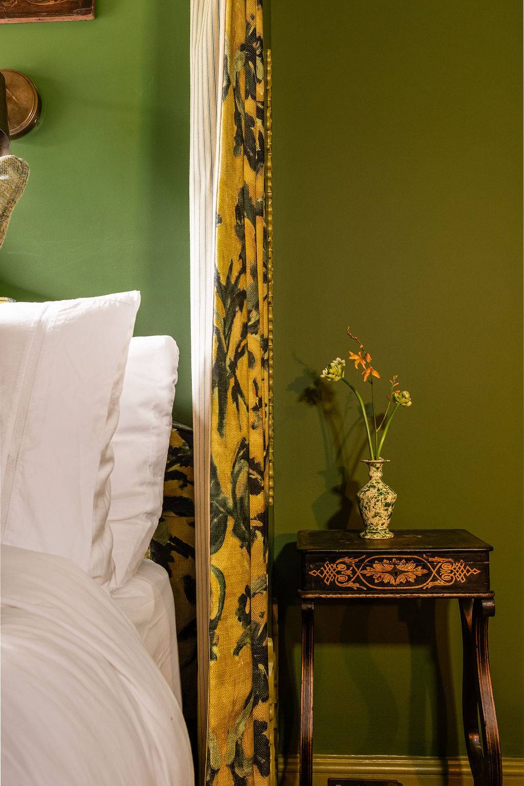 Close-up vignette of a bed flanked by luxurious black and gold baroque style drapes, an editorial design backdrop via Love Locations.