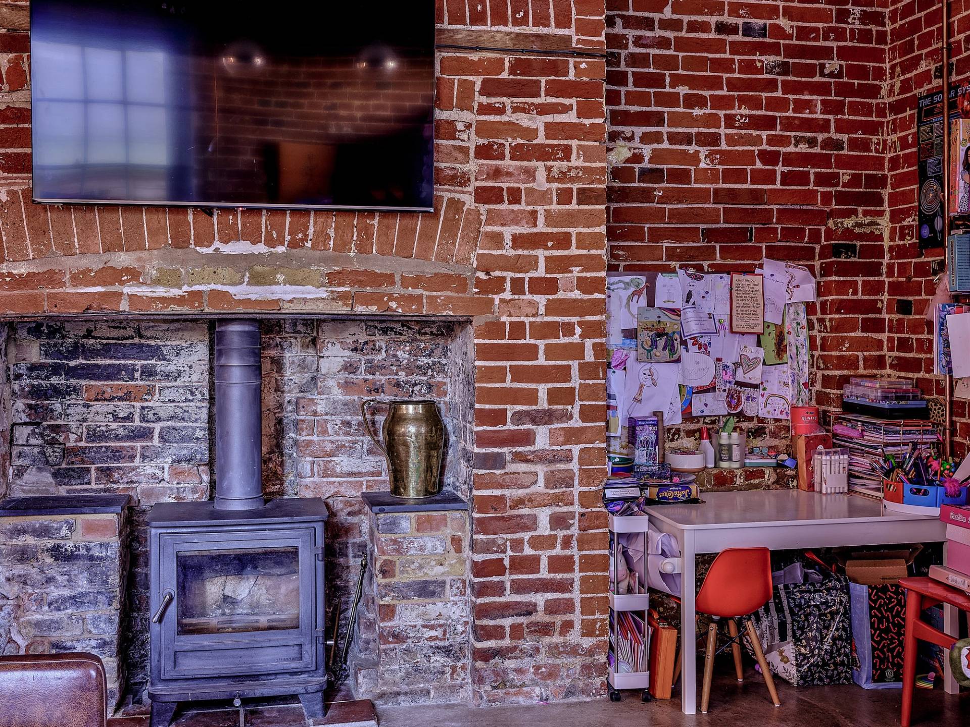 Log-burning stove set in a red brick fireplace alcove with rustic desk and brickwork walls, perfect for cozy autumn campaigns, Love Locations.