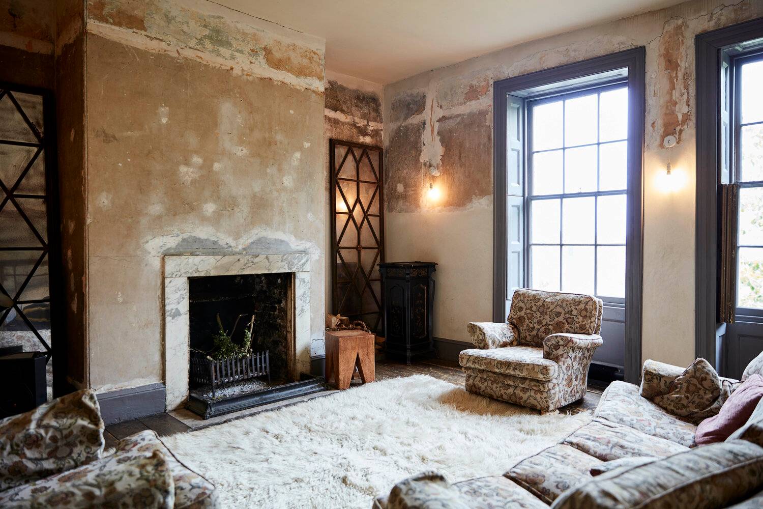 Rustic living room corner showcasing distressed plaster walls, a marble fireplace surround, and vintage seating, ideal for artistic film scenes, Love Locations SE8.