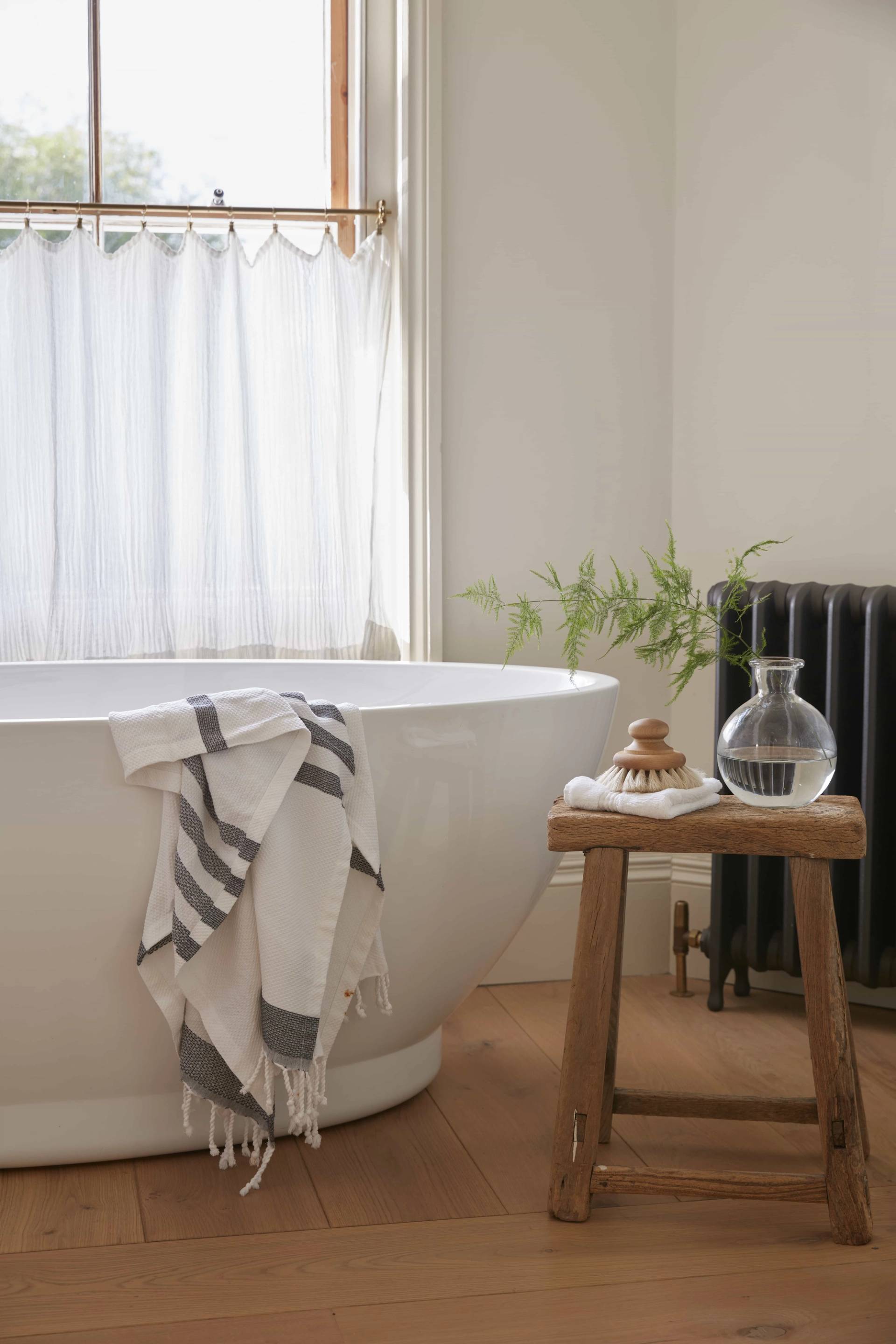 Close-up detail of a white soaking tub, wooden stool, and bathroom accessories, Love Locations TN34.