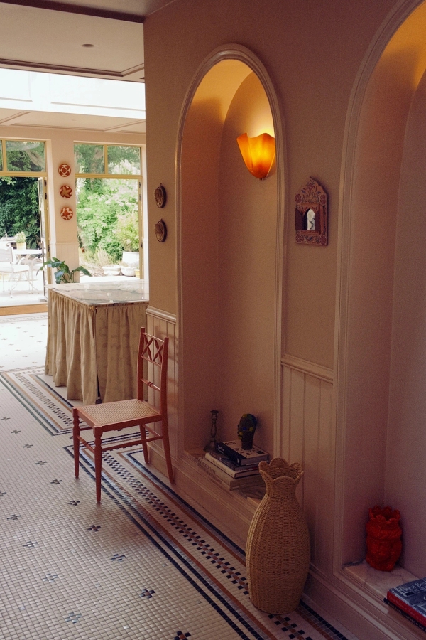 Warm interior hallway view looking past a traditional red chair toward a sunlit conservatory dining area, Love Locations West London.