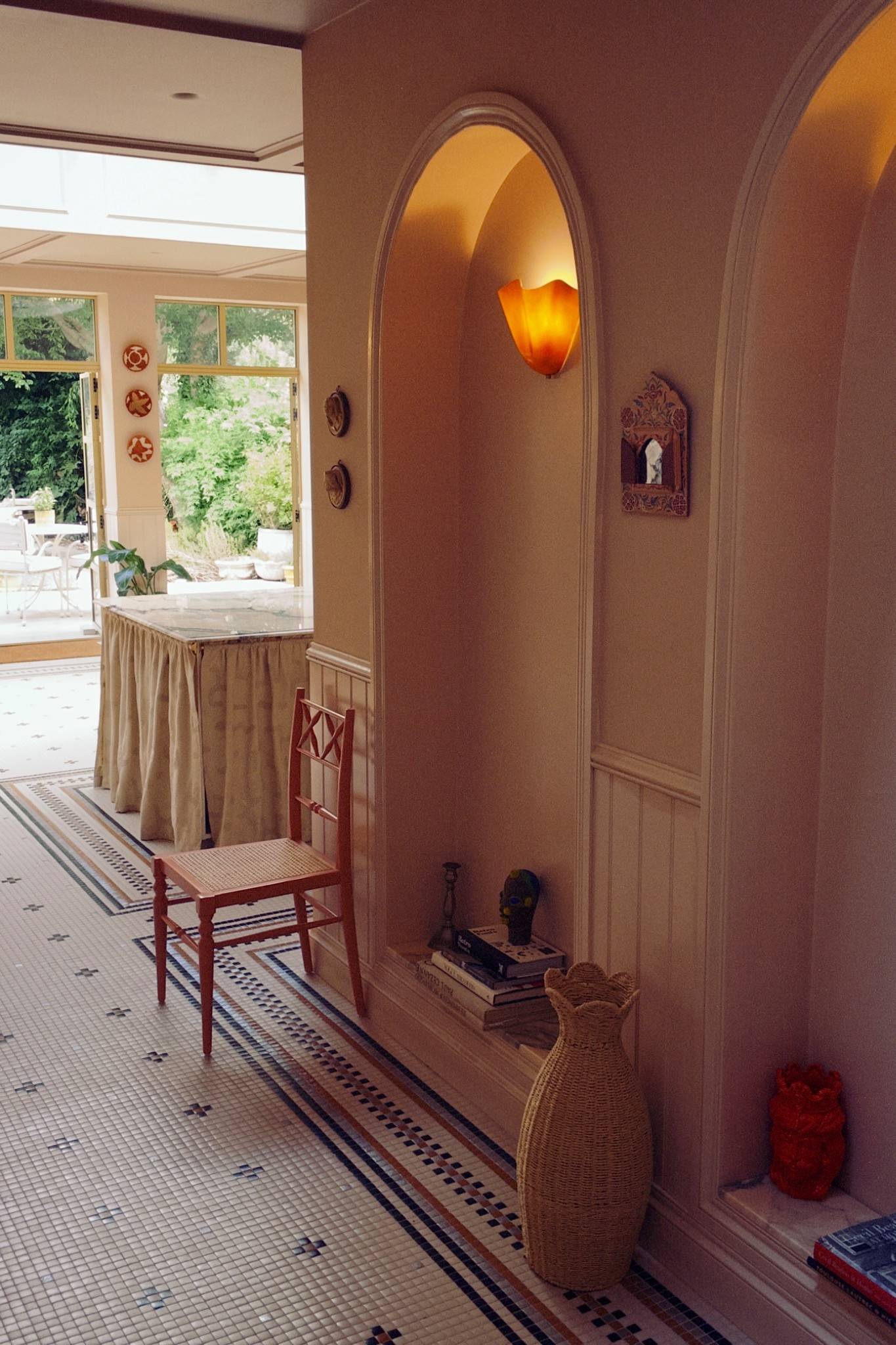 Warm interior hallway view looking past a traditional red chair toward a sunlit conservatory dining area, Love Locations West London.