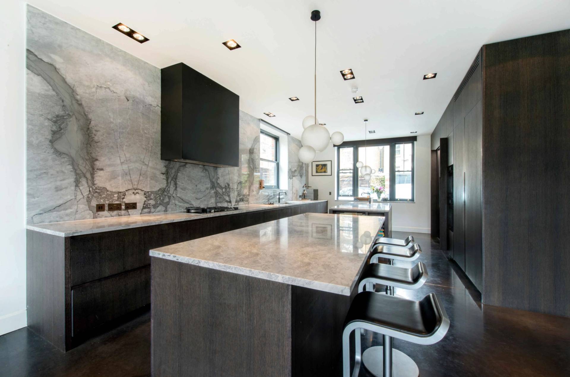 Modern kitchen island featuring a marble stone countertop, bar stools, and dark cabinetry in a luxury Belsize Park home, Love Locations NW3.