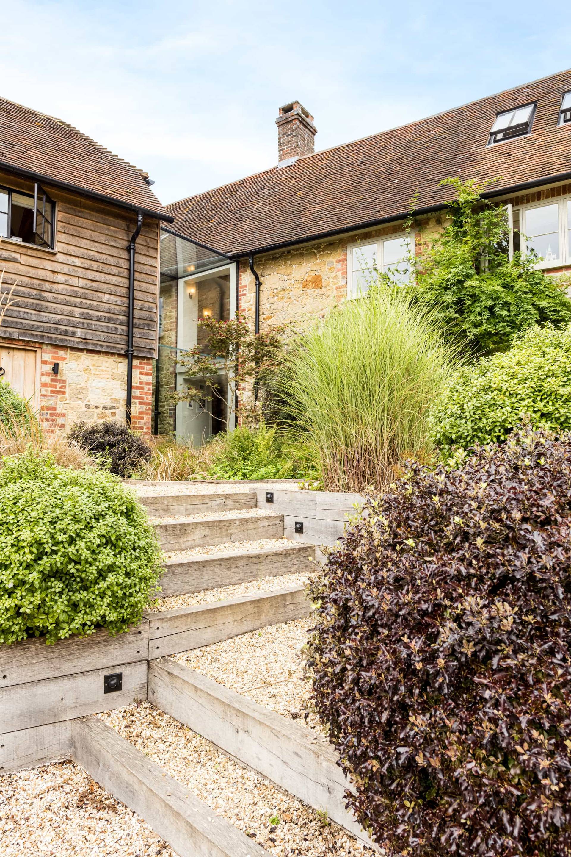 Terraced stone garden steps leading up to a glass link entrance surrounded by lush green shrubs, Love Locations GU28.