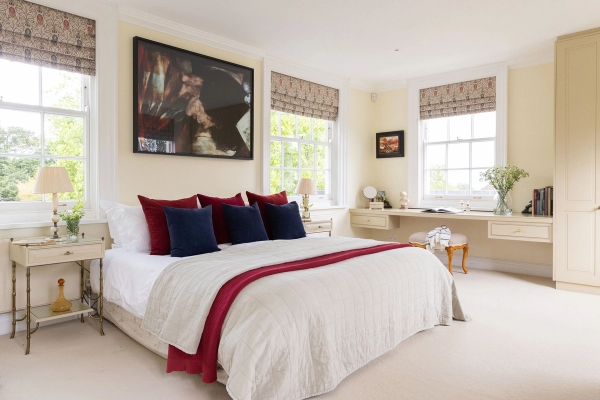 Love Locations curated bedroom studio Steyning: Light-filled neutral bedroom featuring deep red accent cushions, a modern canvas mural, and a dedicated window writing desk.