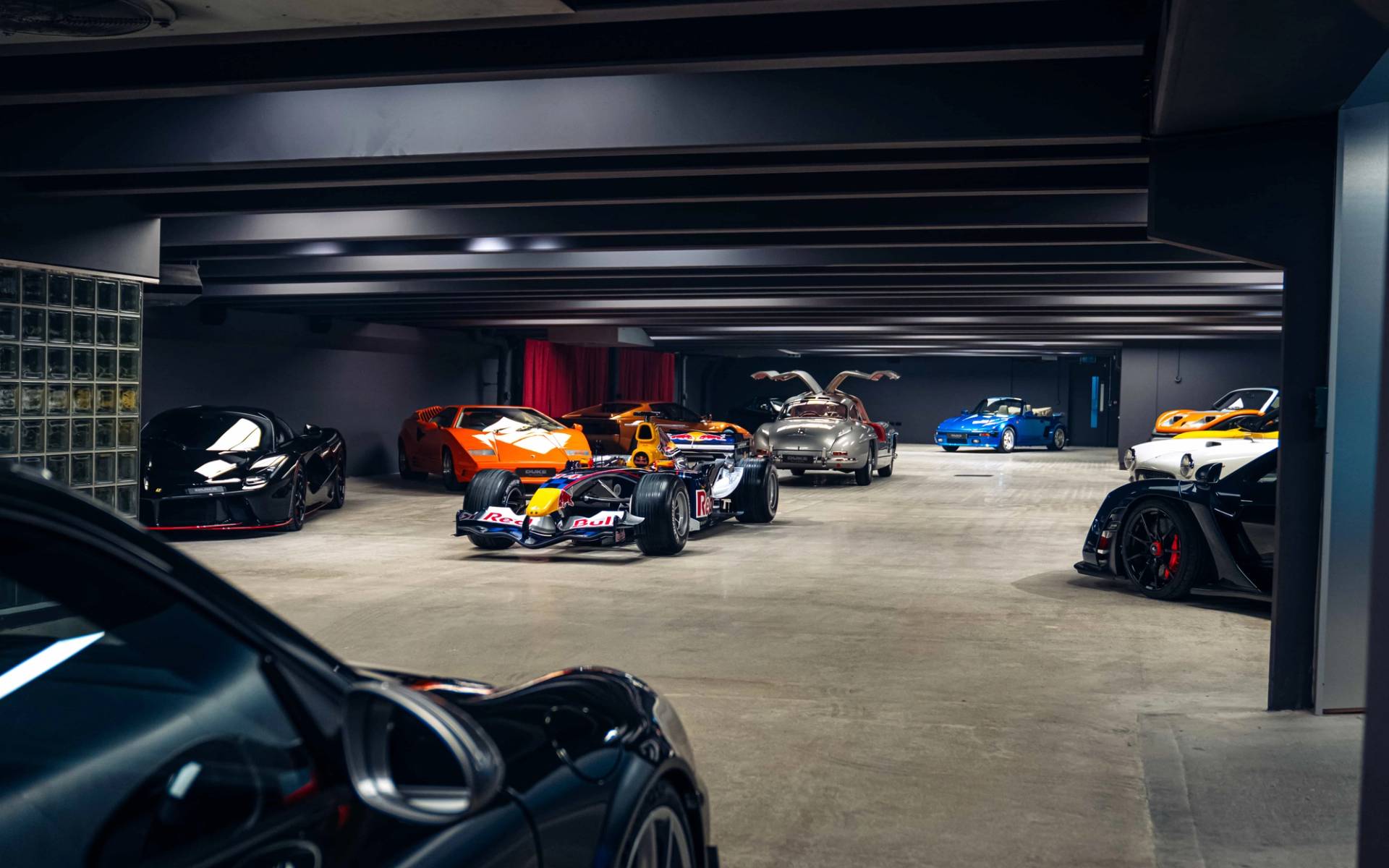 Wide open underground showroom space featuring a Formula 1 car and luxury sports vehicles in Brentford TW8 via Love Locations.