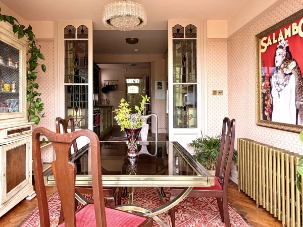 Eclectic dining nook with glass table, wooden chairs, and stained glass doors in an Edwardian home, Love Locations N13.