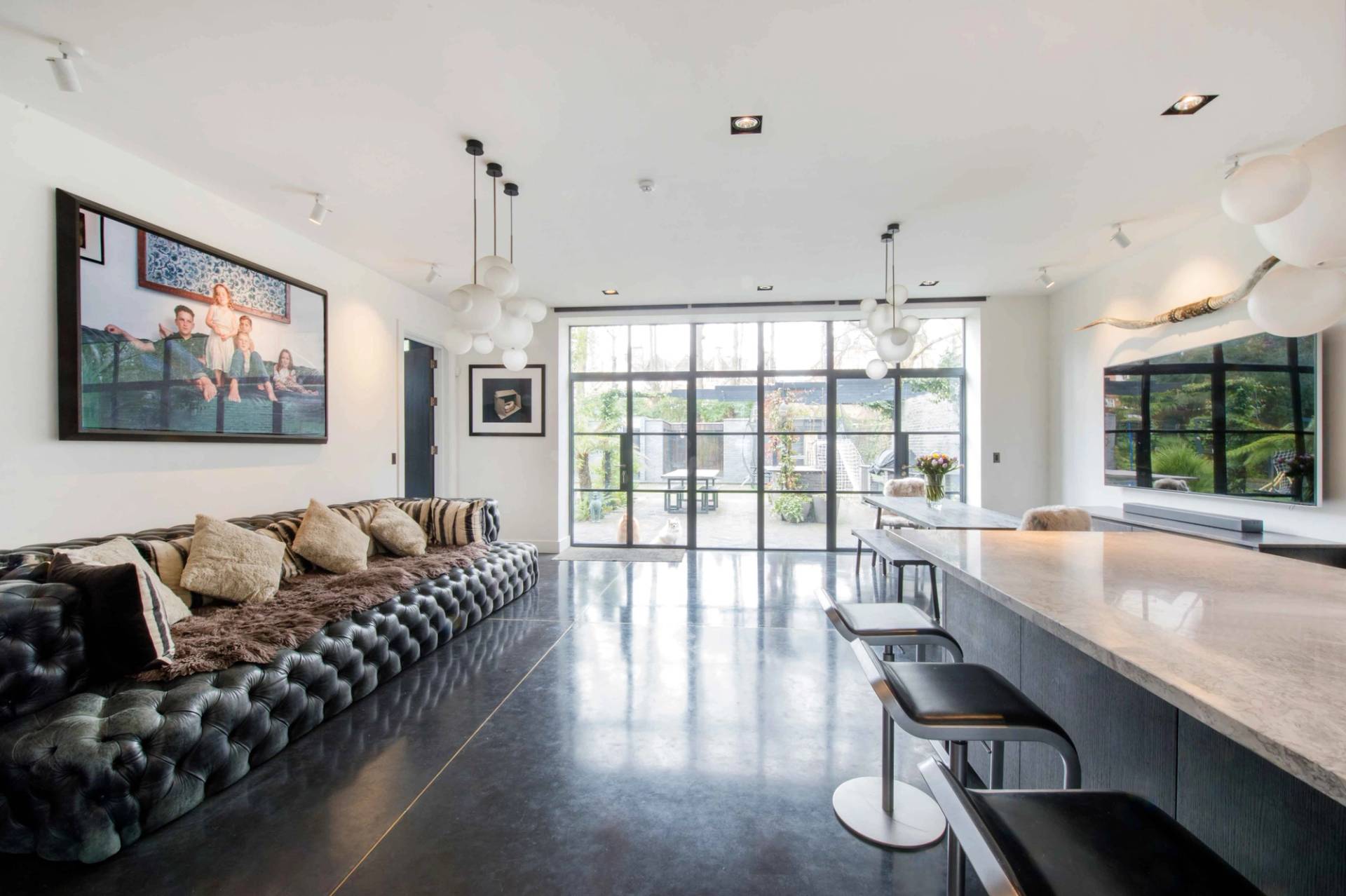 Open-plan kitchen and breakfast bar area looking out through large rear glass doors toward the garden, Love Locations NW3.
