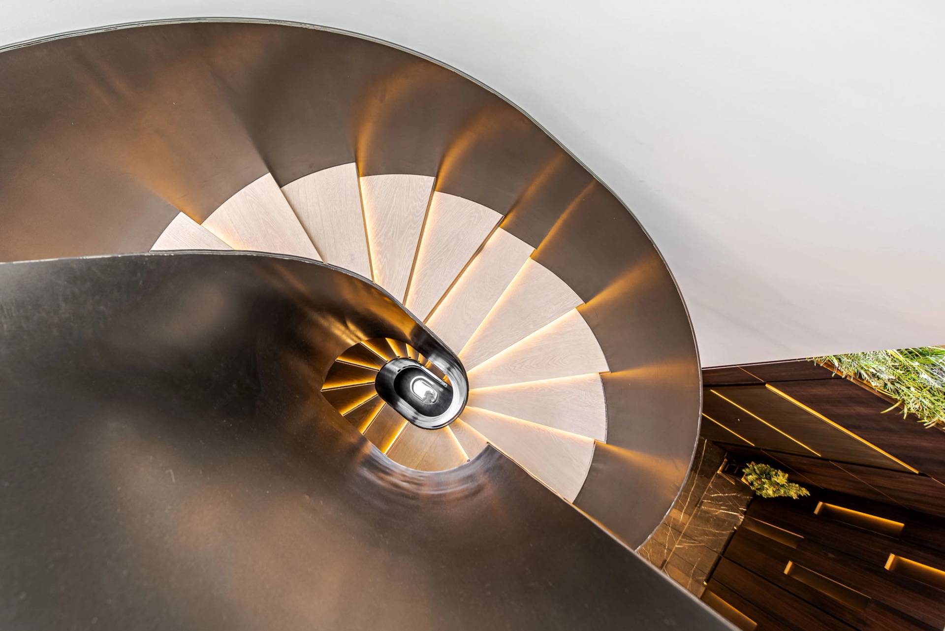 Top-down spiraling view of a luxury dark metal helical staircase illuminated by LED step lights, Love Locations SW11.