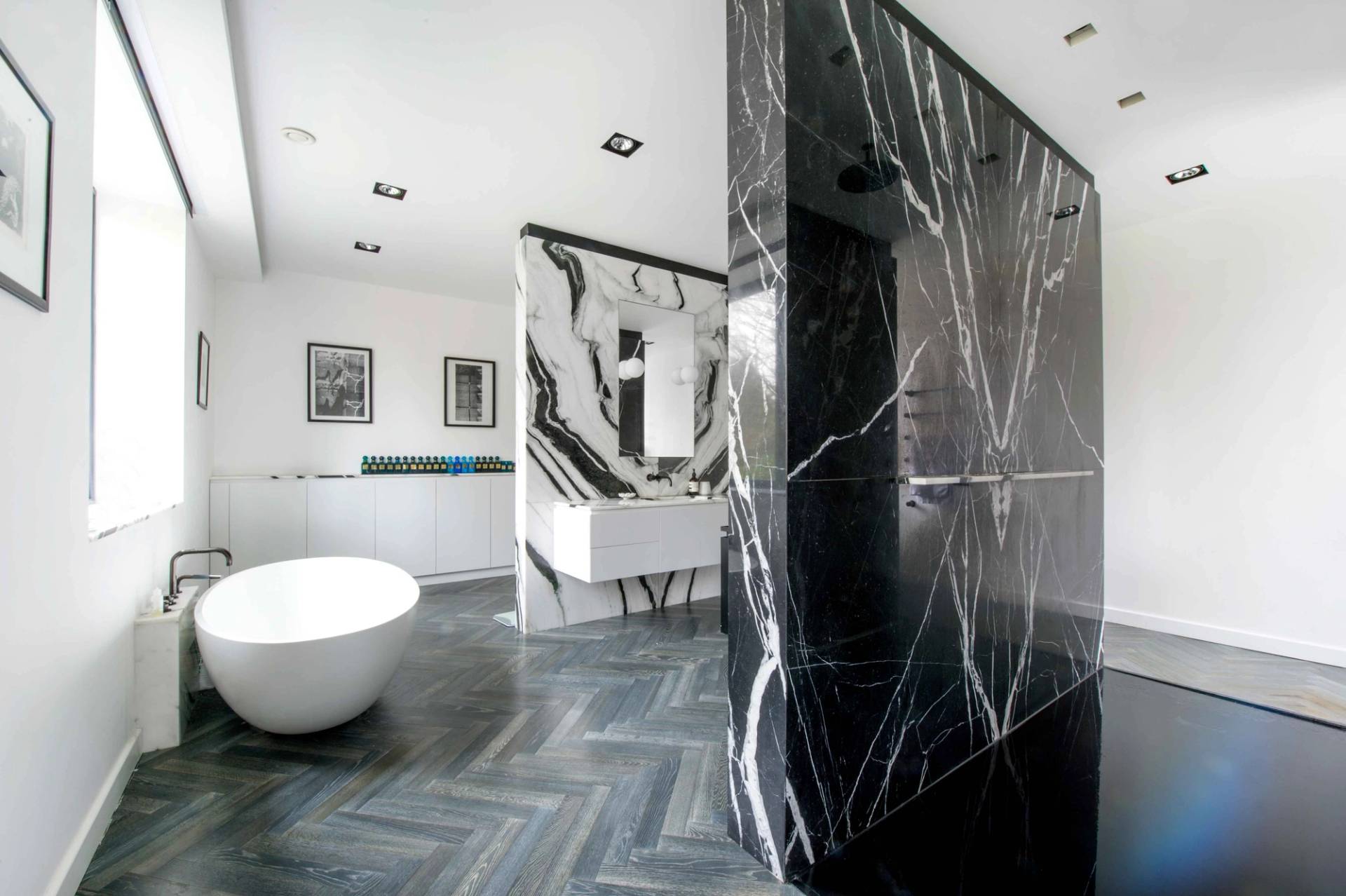 Architectural bathroom design featuring a striking black marble walk-in shower wall and polished herringbone flooring, Love Locations NW3.