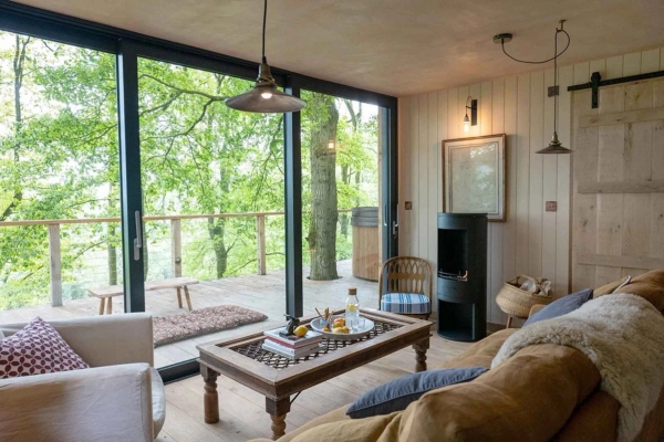 Bright living area looking through large dark-framed sliding glass doors out to a lush green forest deck backdrop, premium editorial shoot space by Love Locations.