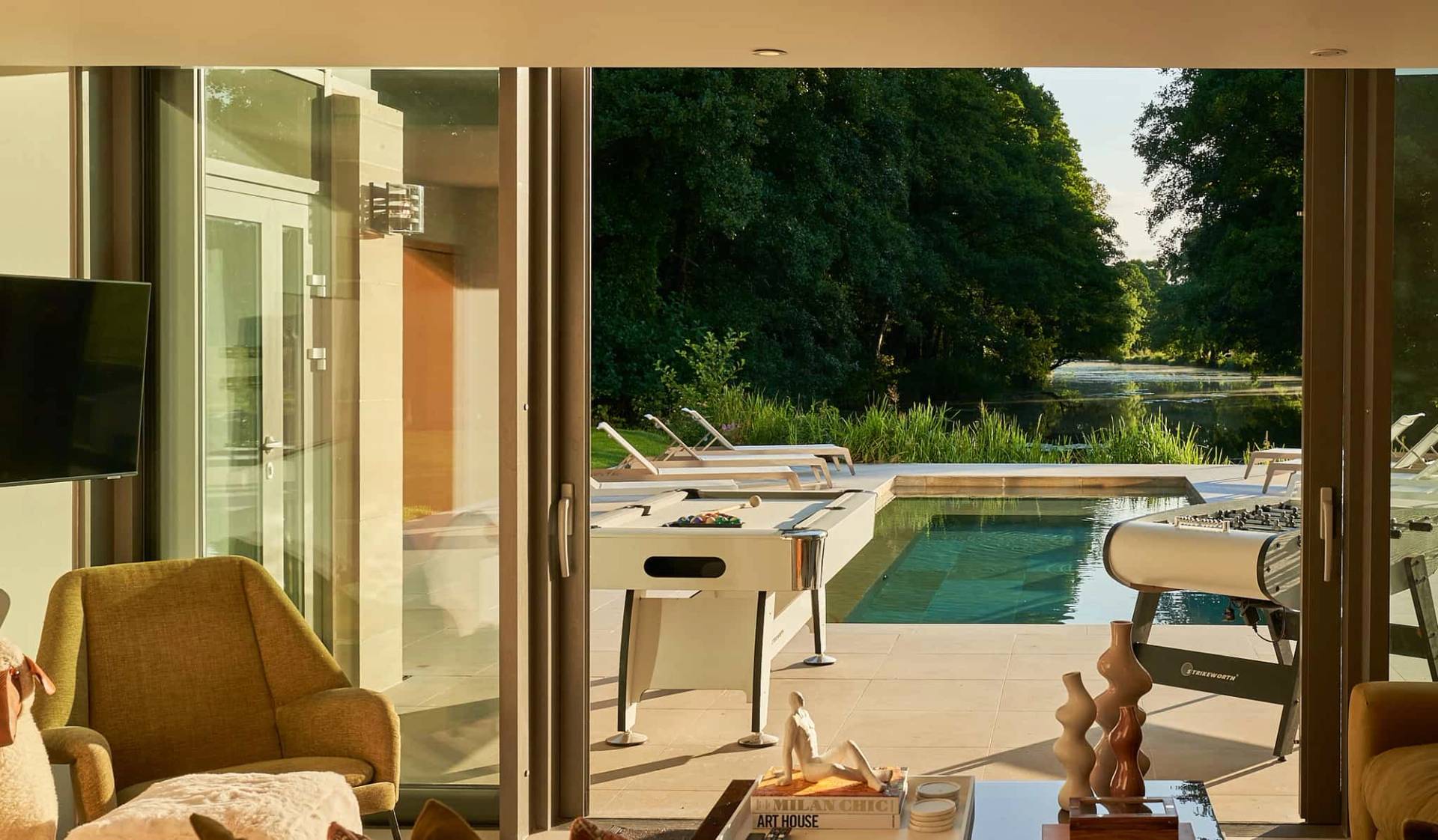 View looking out from a pool house room onto an outdoor swimming pool and sun loungers, Love Locations SO21.