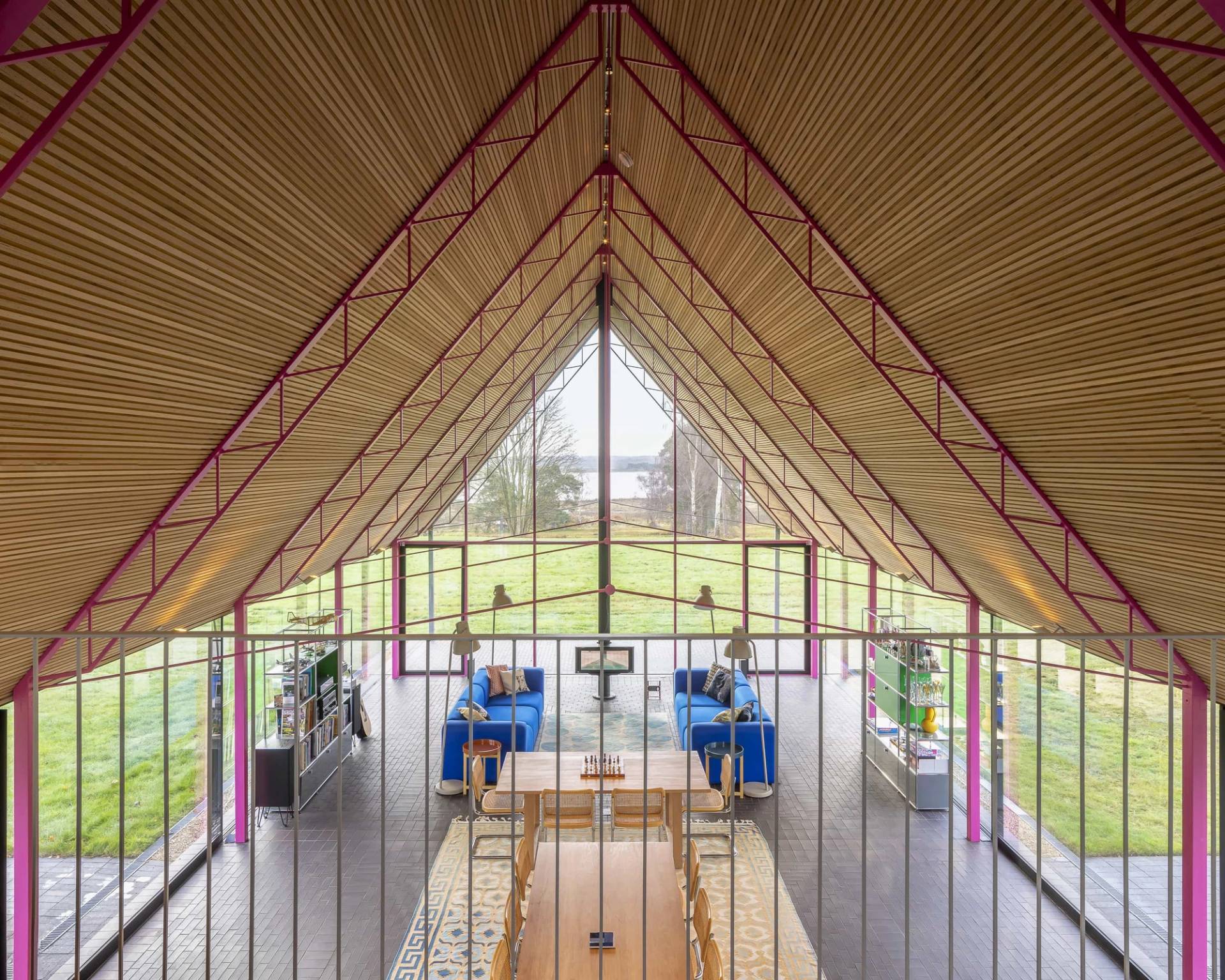 Symmetrical view along the central axis of a modern thatched longhouse with pink steel framework and polished concrete floors, Love Locations IP17.