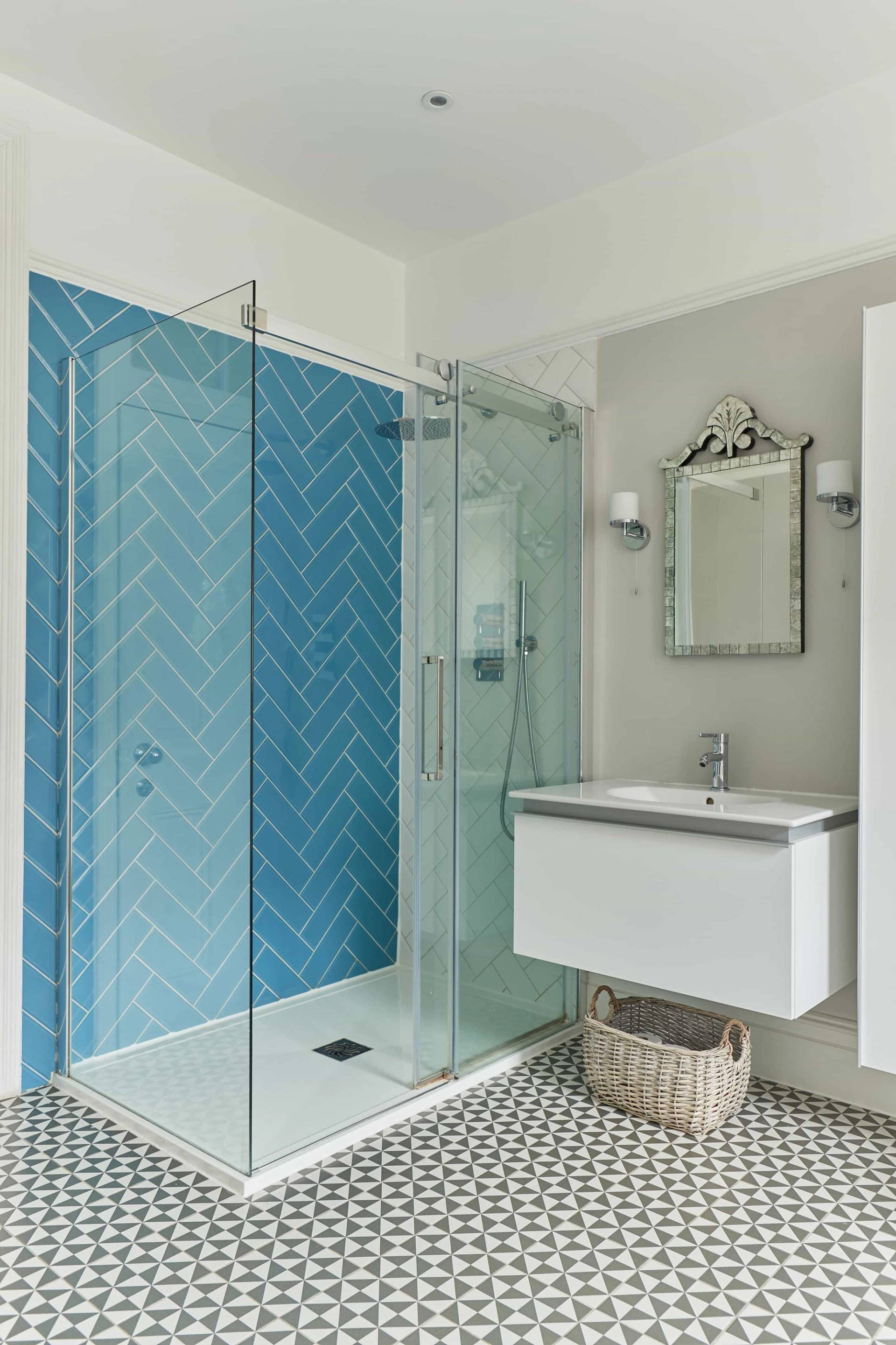 Modern walk-in shower enclosure featuring bright blue herringbone tile walls, white vanity unit, and silver fixtures, Love Locations W3.