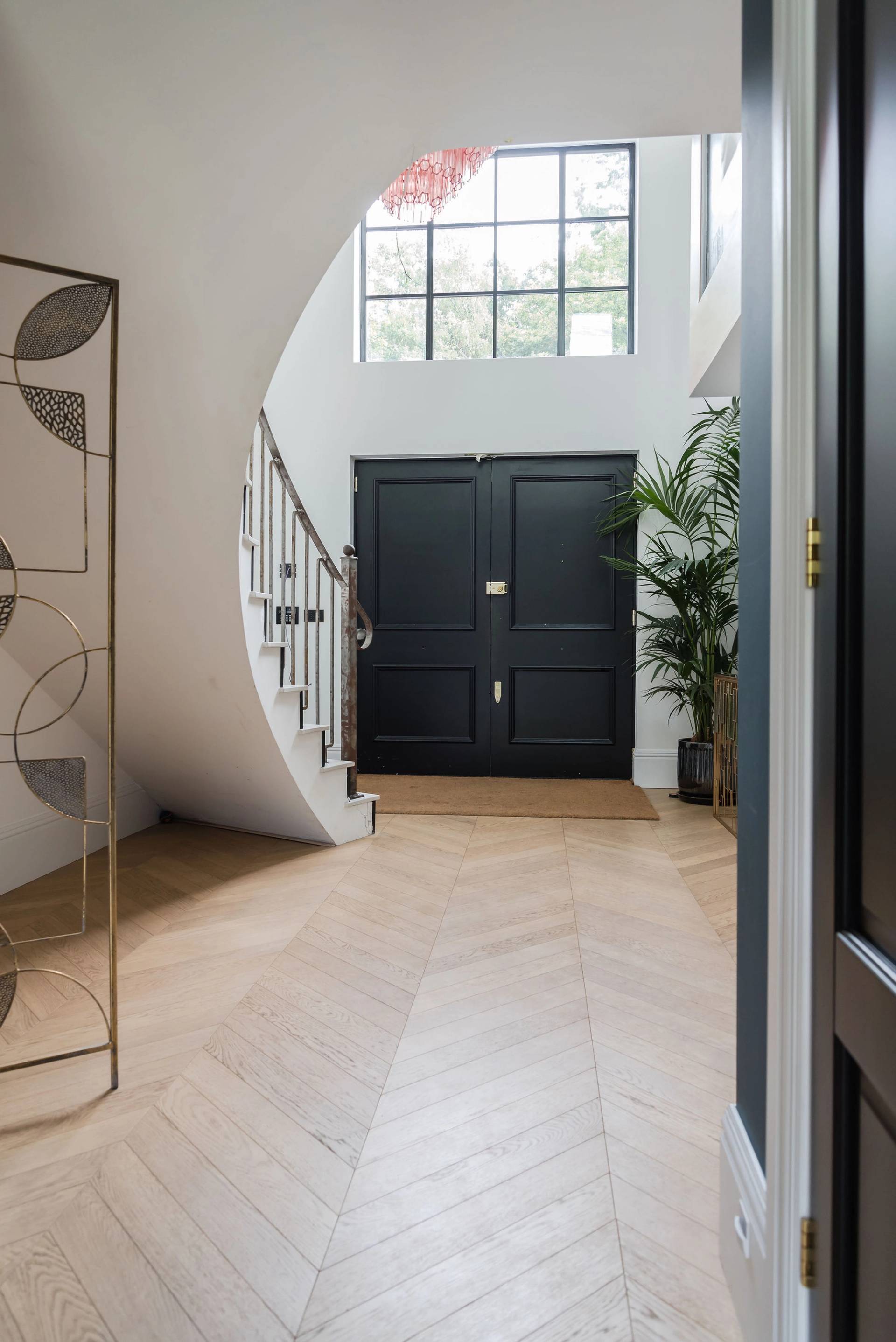 Grand double-height entrance foyer with double black front doors, large window, and bespoke curved metal staircase, Love Locations GU3.