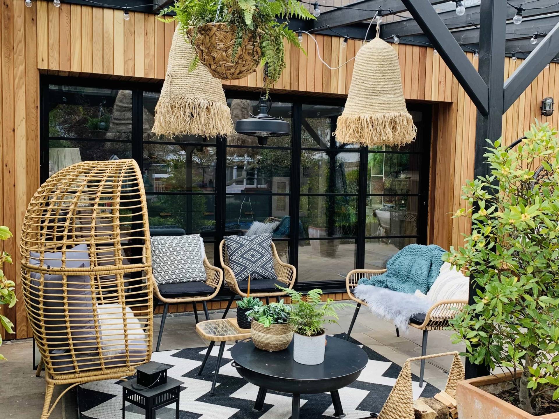 Outdoor living lounge set under a glass-roofed pergola with monochrome geometric rug and rattan seating, Love Locations TW11.