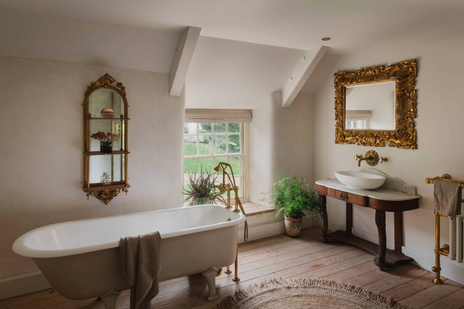 Luxury bathroom location featuring a freestanding clawfoot tub, gold fixtures, and ornate mirrors in a Cornish manor via Love Locations.