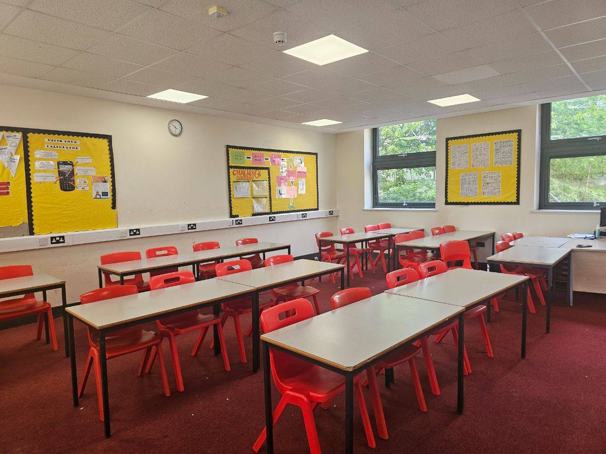 Empty high school classroom shoot location with rows of student desks, red chairs, and ample natural light, Love Locations Buckinghamshire.