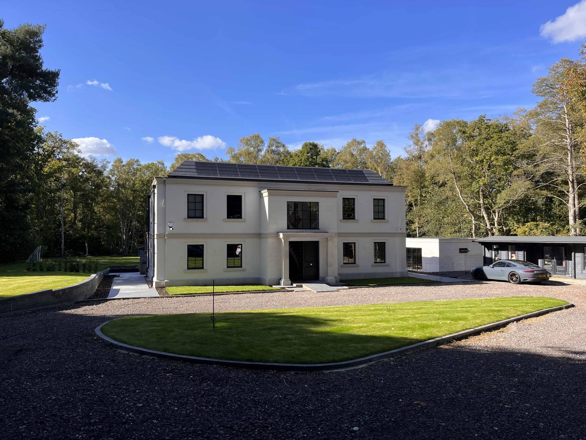 Wide shot of a luxury white modern mansion facade set behind a spacious gravel entrance courtyard in GU3, Love Locations.
