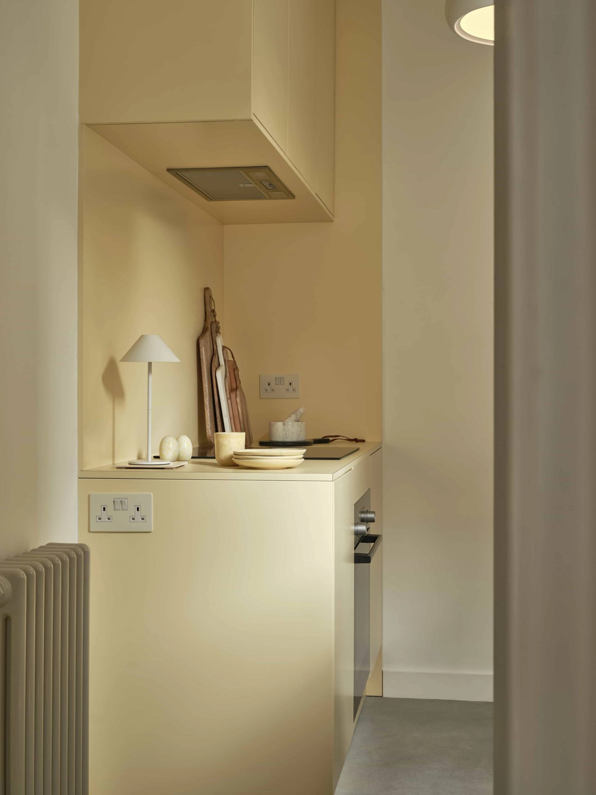 Buttercream yellow kitchen view showcasing minimalist upper cabinetry and built-in extractor hood, Love Locations E4.