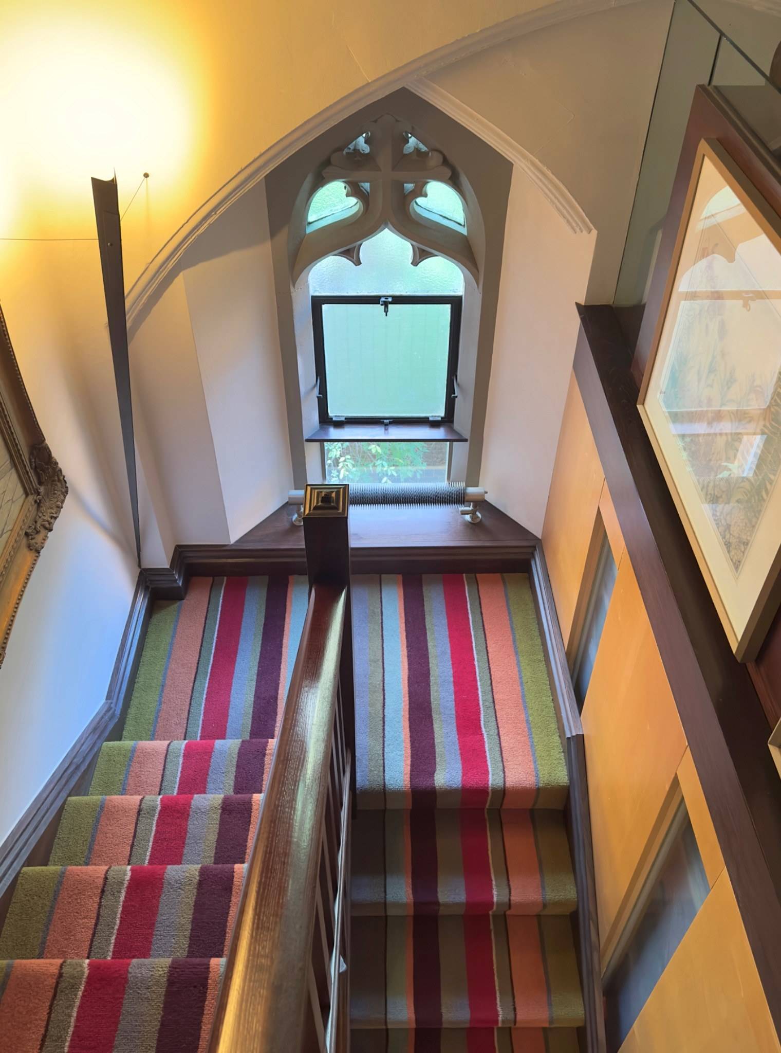 Characterful stairwell with a colorful striped carpet runner leading up to a gothic arched window in Oval SE5 from Love Locations.