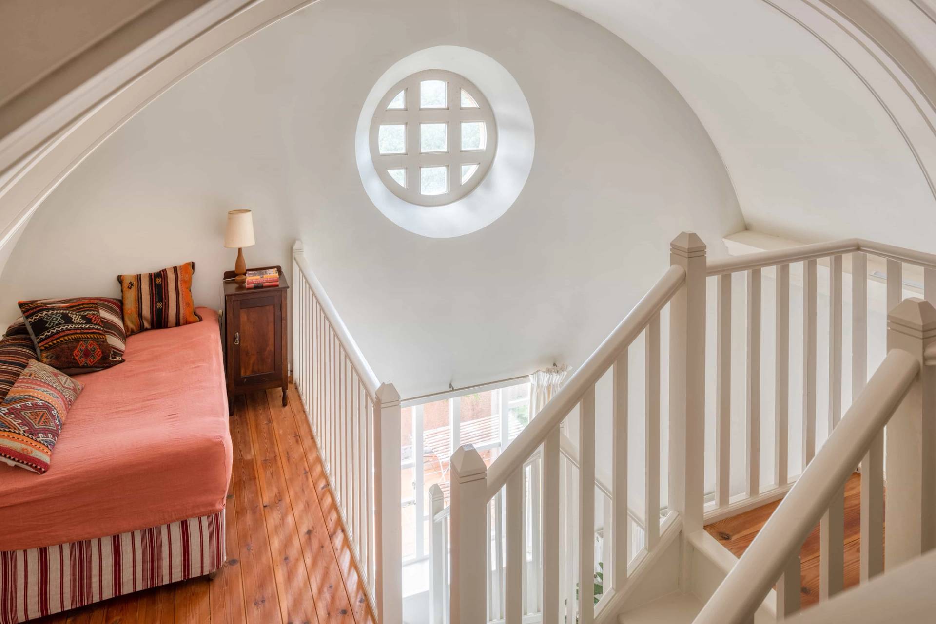 Vaulted stairwell landing area featuring a circular porthole window and white balustrade in a luxury home through Love Locations.