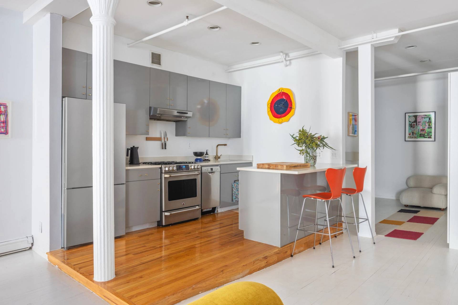 Open-plan kitchen filming venue in a white Tribeca loft via Love Locations, showcasing stainless steel appliances, grey cabinetry, and orange high-top stools.