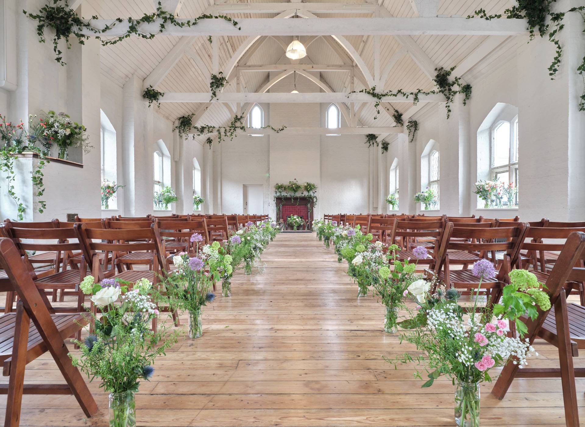 Symmetrical aisle view of a wedding ceremony setup with wooden chairs and floral arrangements in a Shoreditch hall venue, Love Locations E2.