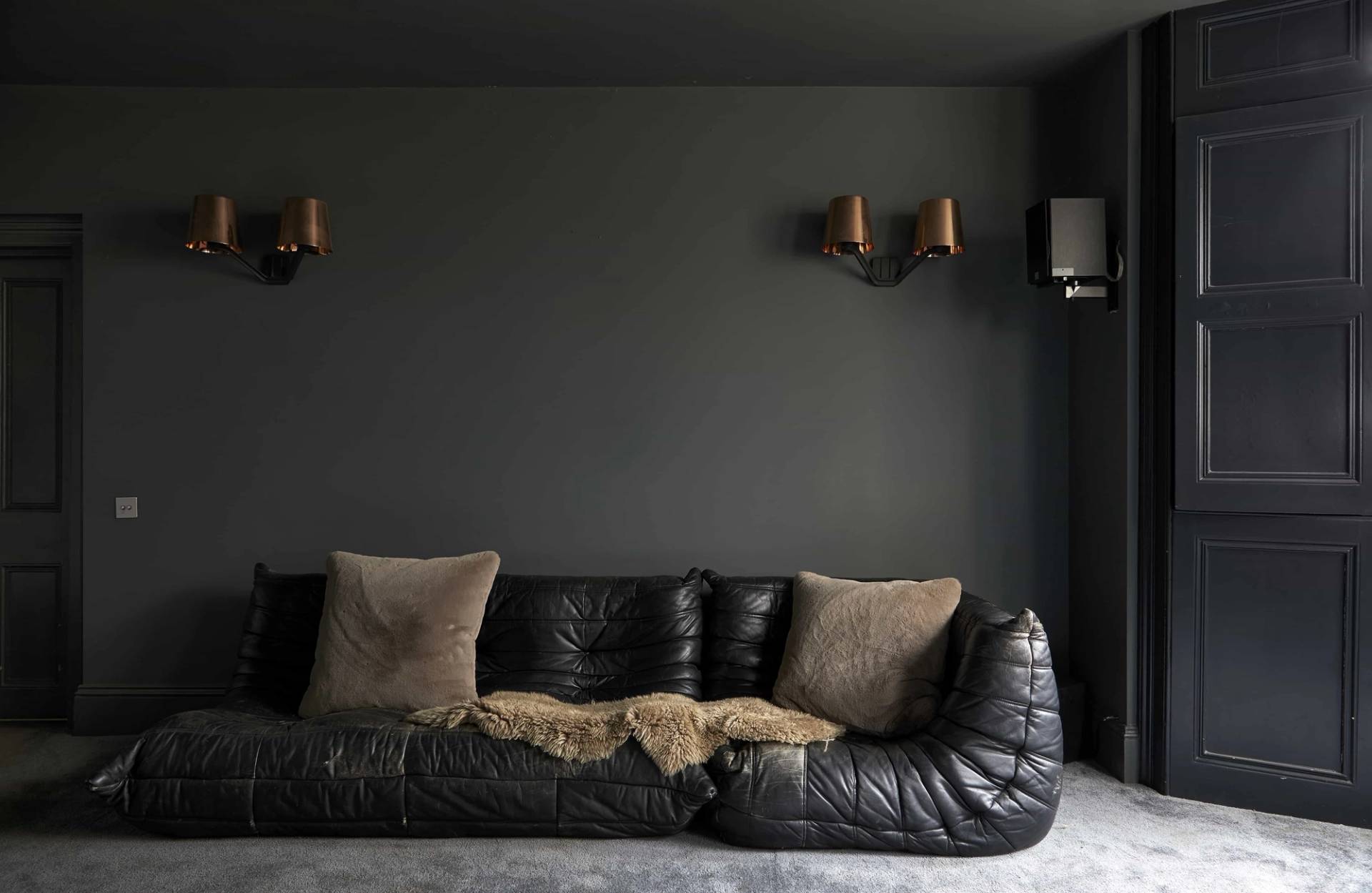Black leather sectional sofa set against deep grey walls with brass wall sconce lights, ideal for drama filming, Love Locations N16.