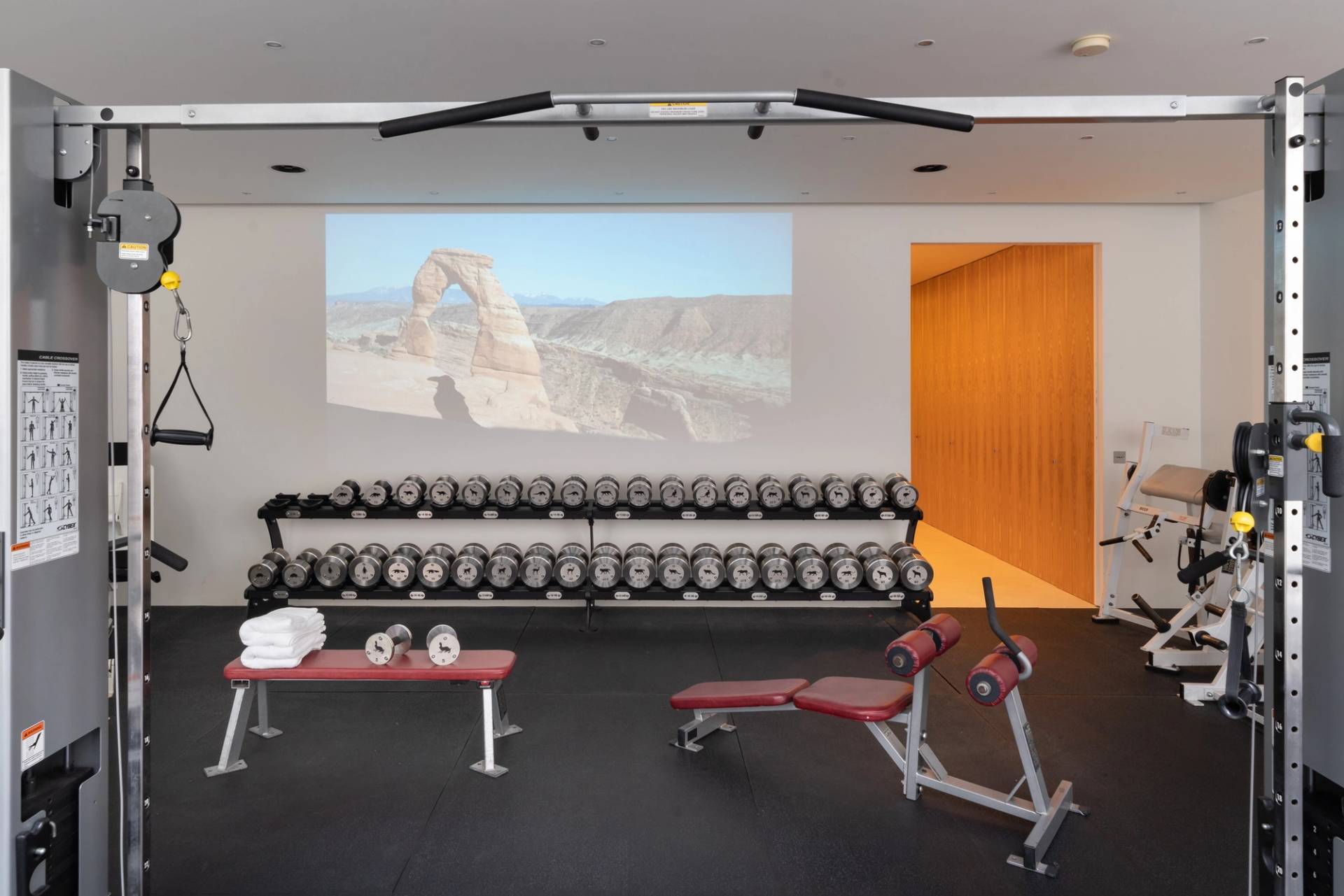 Subterranean gym and media room featuring a projection screen, dumbbell racks, and workout benches, Love Locations SW6.