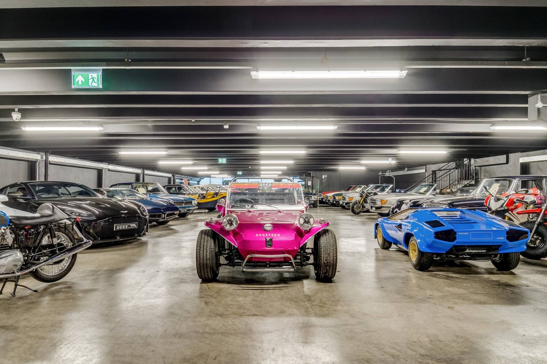 Custom pink dune buggy and sports cars on display in an industrial car showroom by Love Locations.