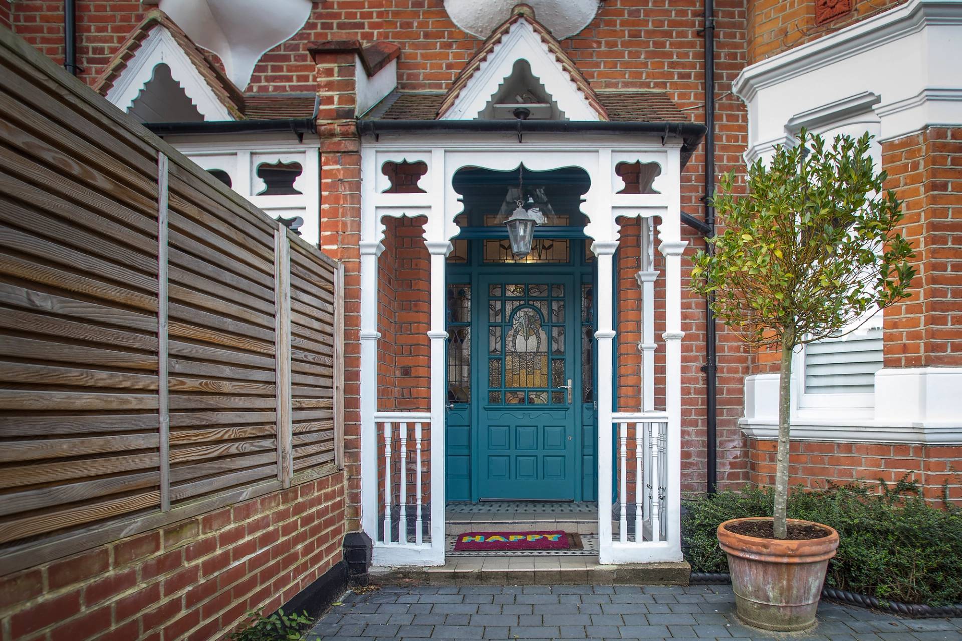 Edwardian front porch facade featuring white decorative timber archways, a teal stained-glass front door, and tiled path, Love Locations.