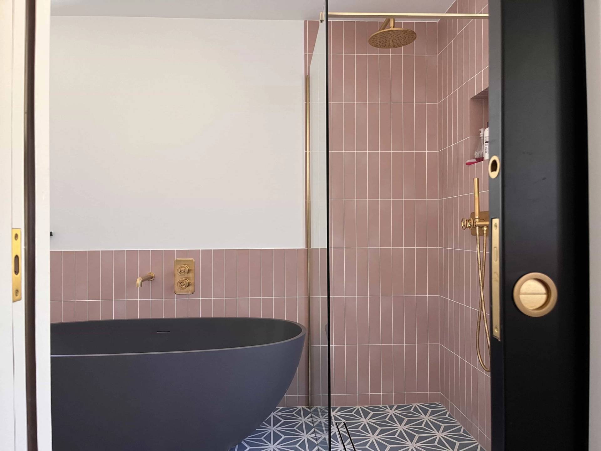 Modern bathroom location featuring a freestanding charcoal bathtub, pink vertical tile wall, and patterned floor tiles, Love Locations GU3.