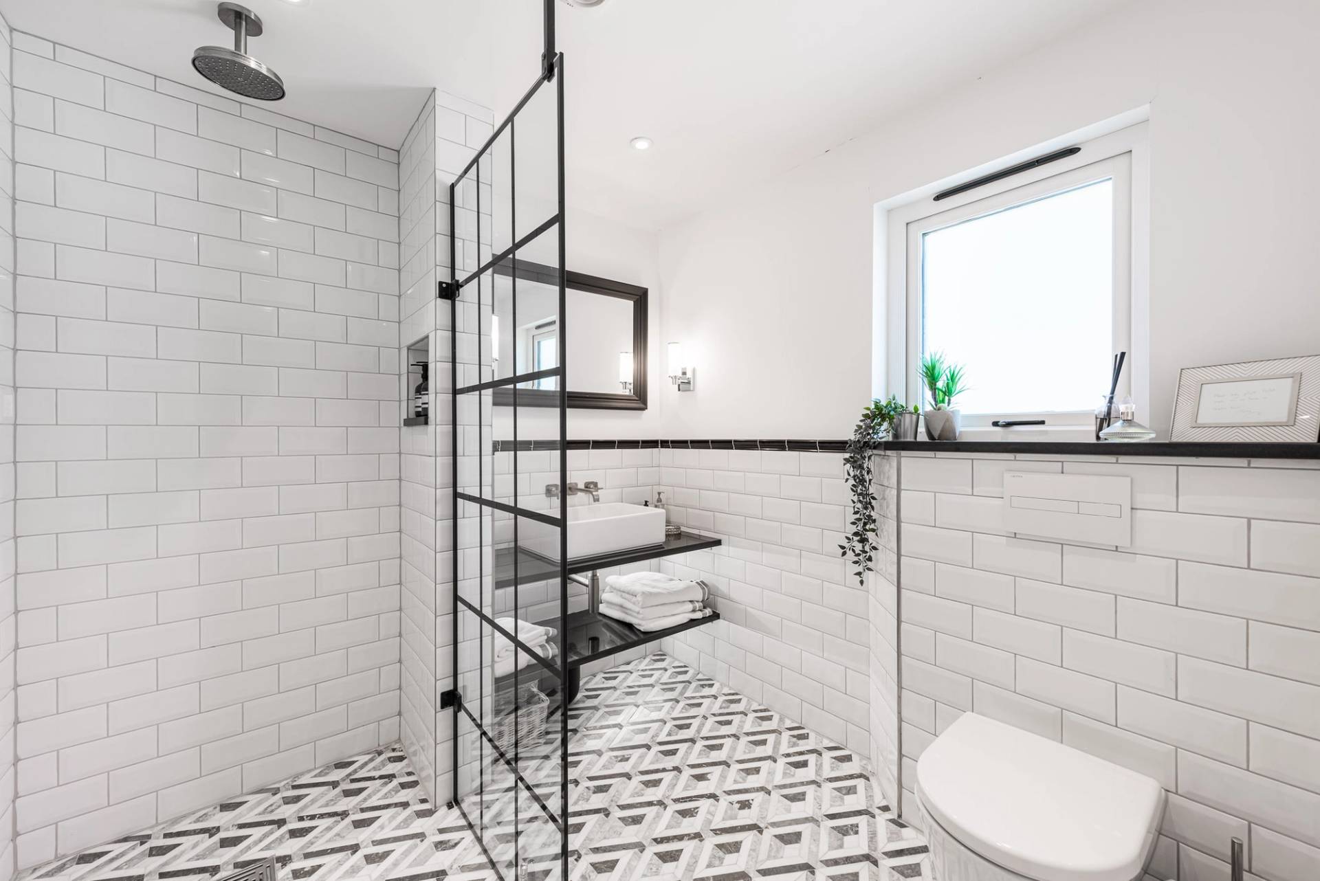 Stylish monochrome walk-in shower room with geometric floor tiles and crittall-style black framed glass doors, Love Locations.
